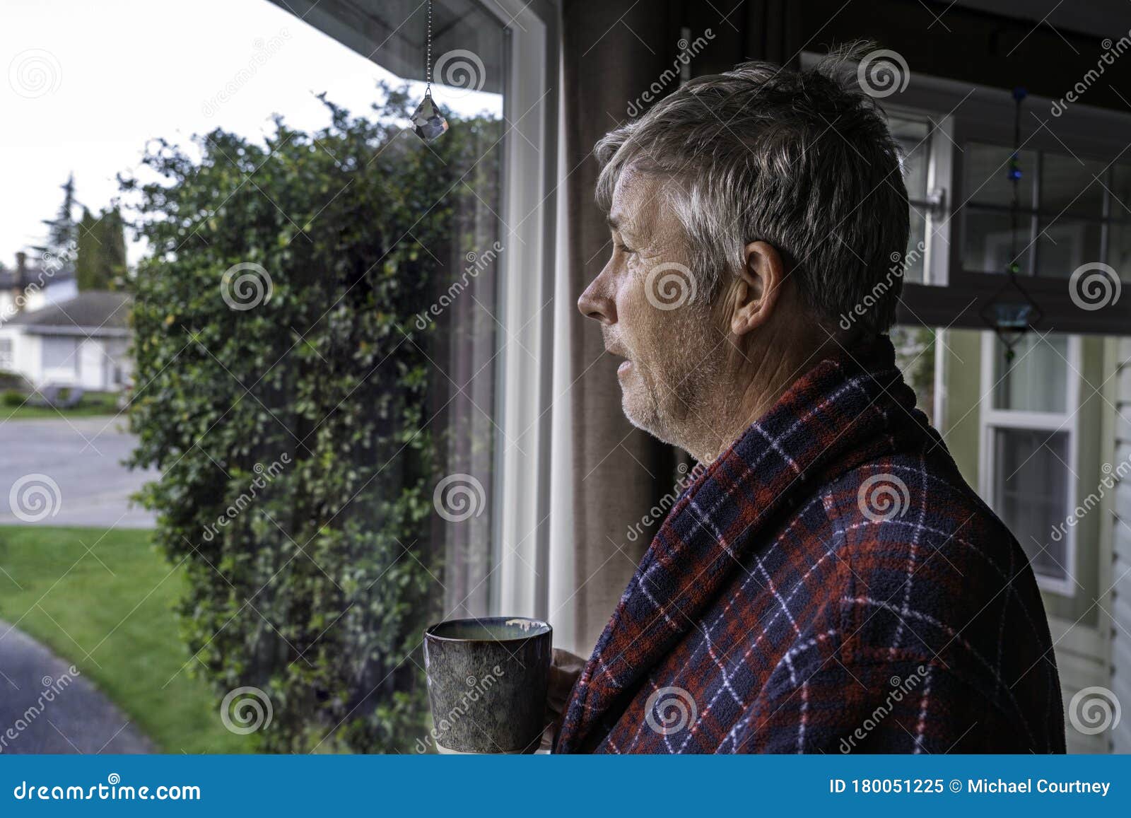 unkept older man with bed head in housecoat looking out window