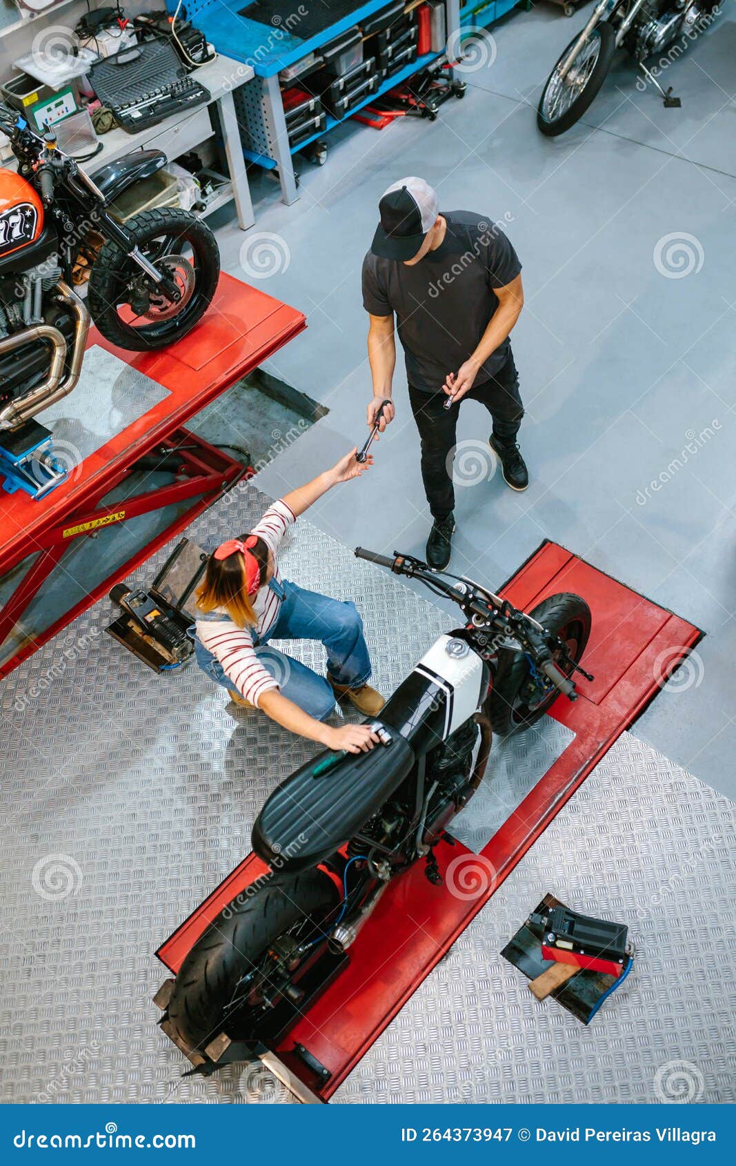 unrecognizable mechanic giving tool to female coworker repairing motorbike on garaje