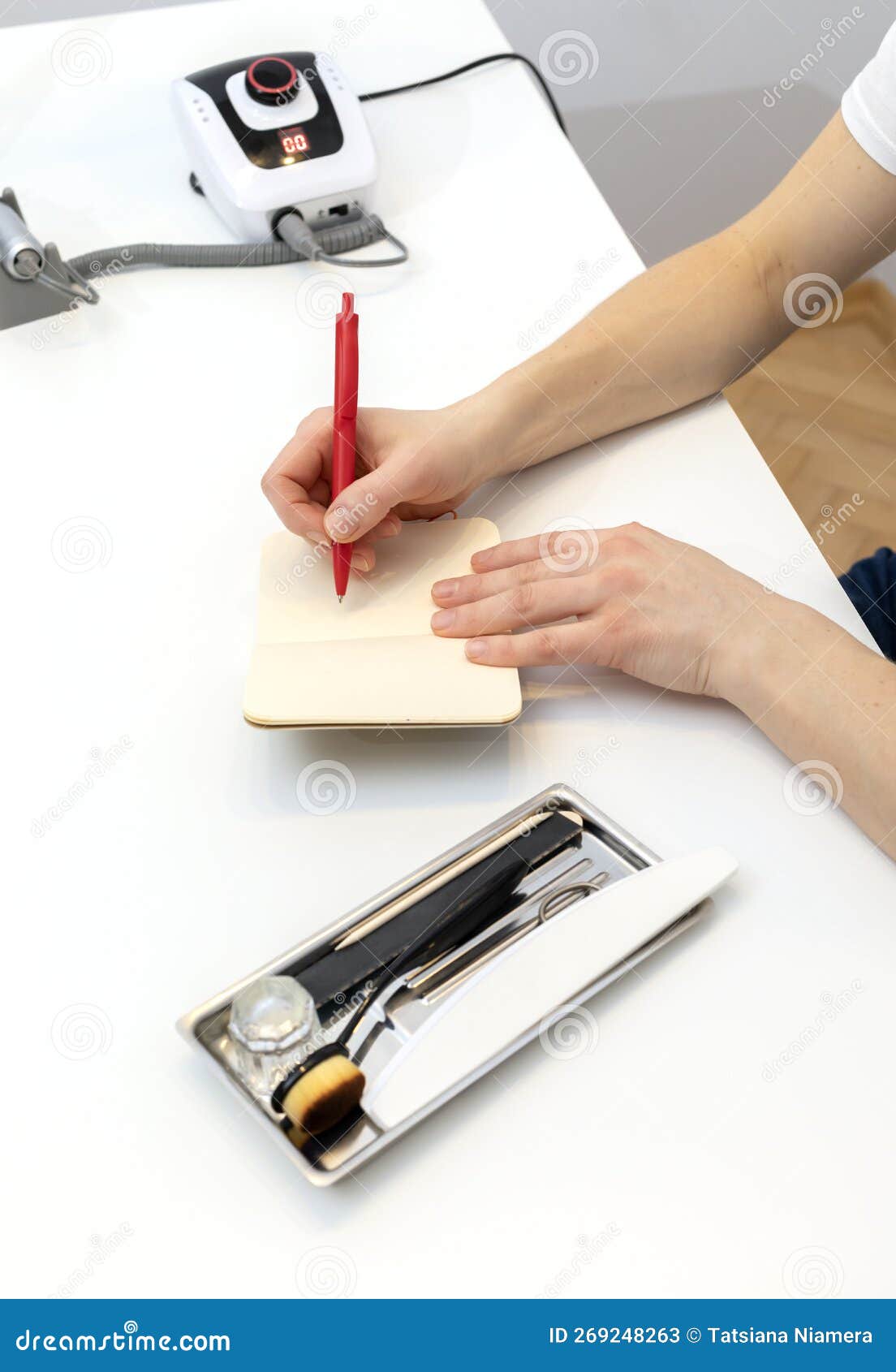 unrecognizable nail master makes notes in notebook with pen, sitting at workstation