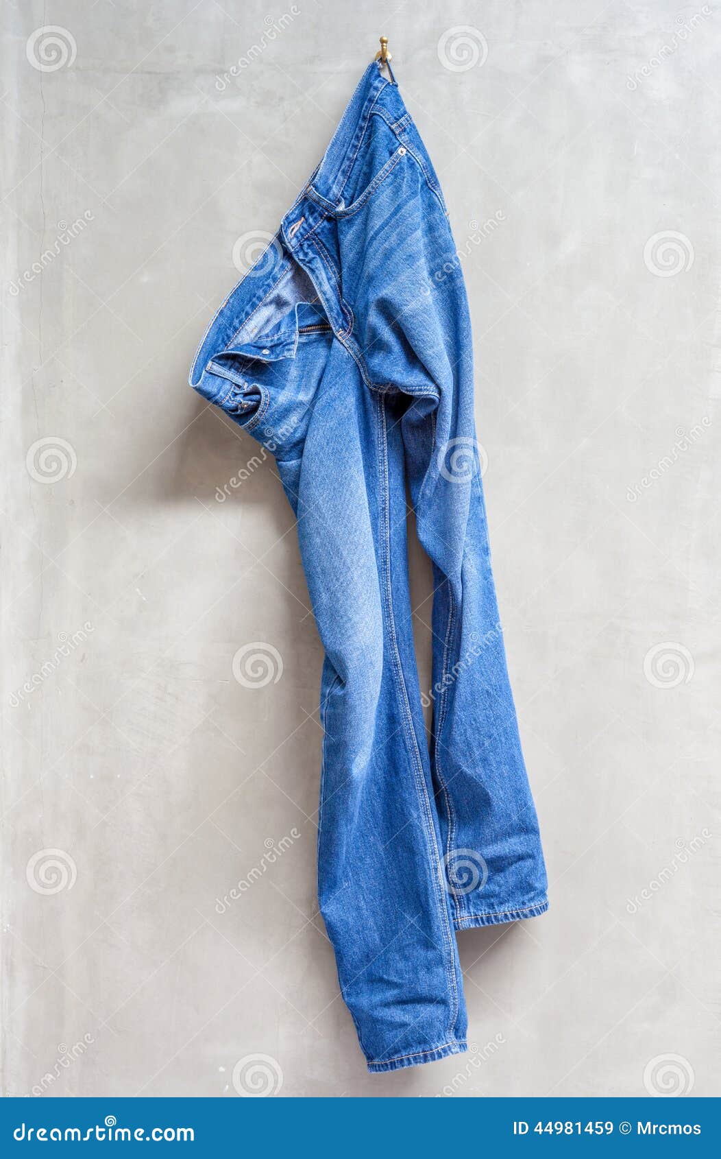 Unwashed Blue Jeans is Hanging on the Exposed Concrete Wall. Stock