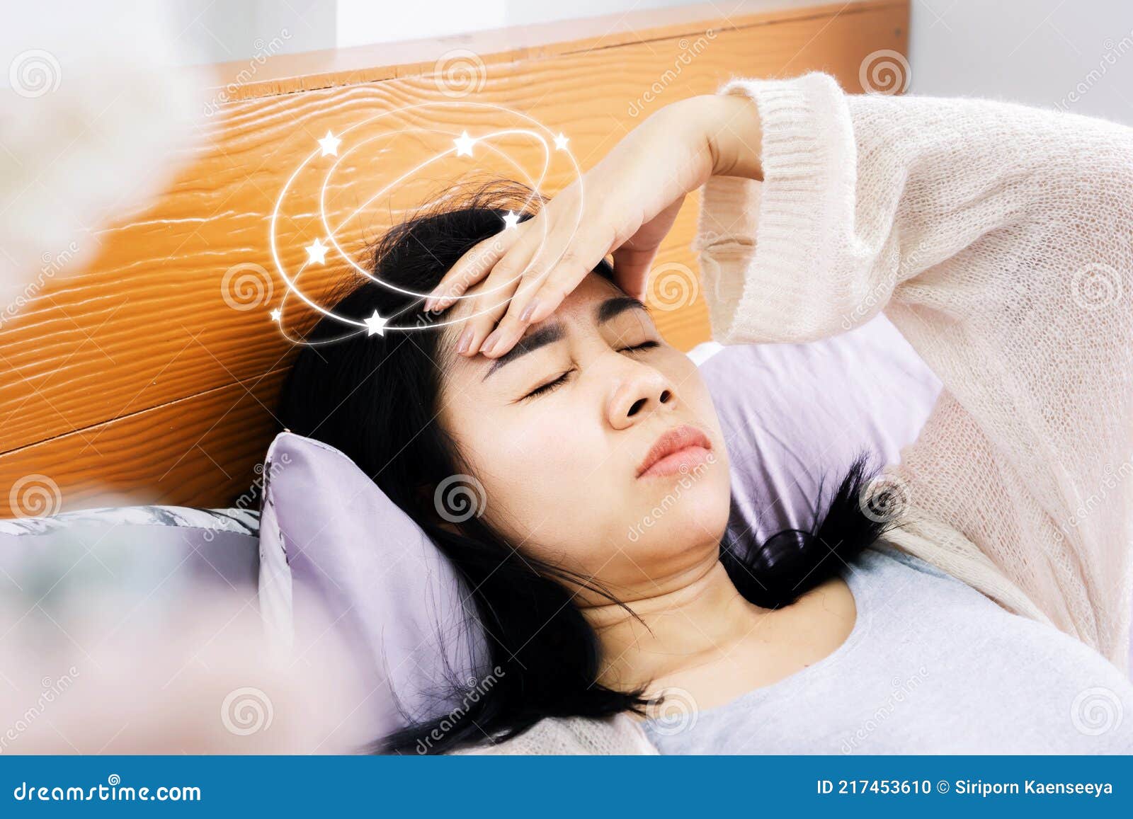 unwell asian woman suffering from dizziness after wakeup in morning hand holding her head lying down in bed