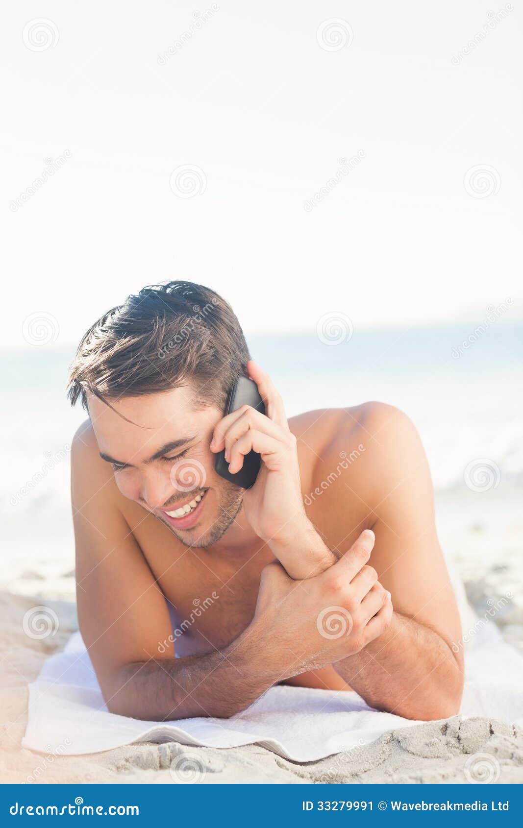 Uomo bello sorridente sulla spiaggia sul telefono. Uomo bello sorridente che si rilassa sulla spiaggia sul telefono