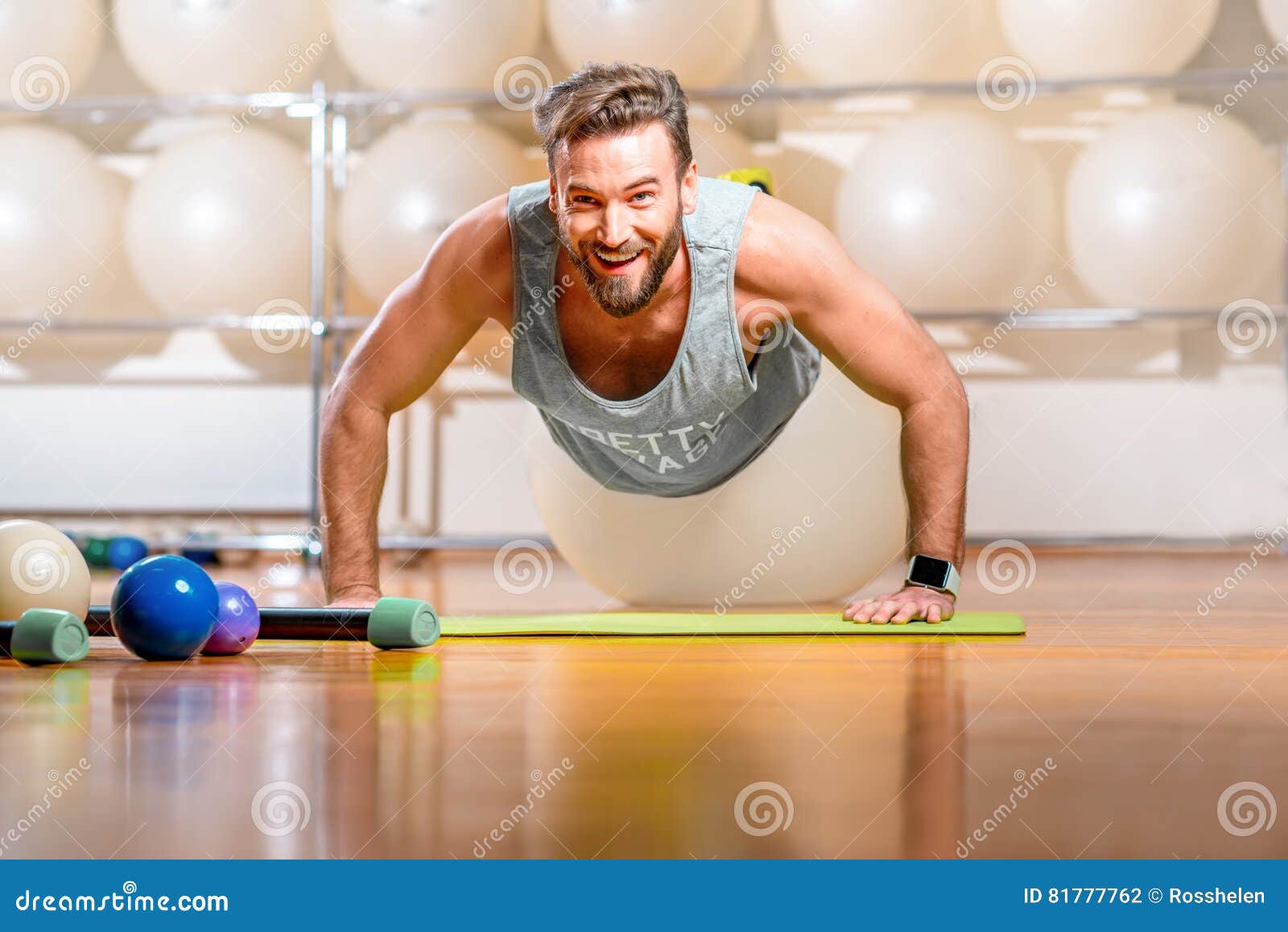 Uomo che si esercita con il fitball. Sorridere mette in mostra l'uomo che fa spinta-UPS con fitball nella stanza di forma fisica