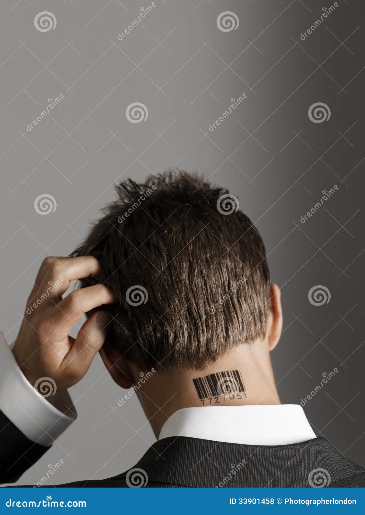 Uomo d'affari With Barcode Tattoo sul collo che graffia il suo capo. Retrovisione di un uomo d'affari con il tatuaggio del codice a barre sul collo che graffia il suo capo contro fondo grigio