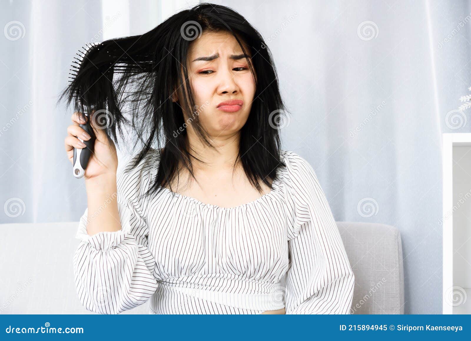 upset asian woman using comp brushing her dry ,damaged hair unhappy with messy hair