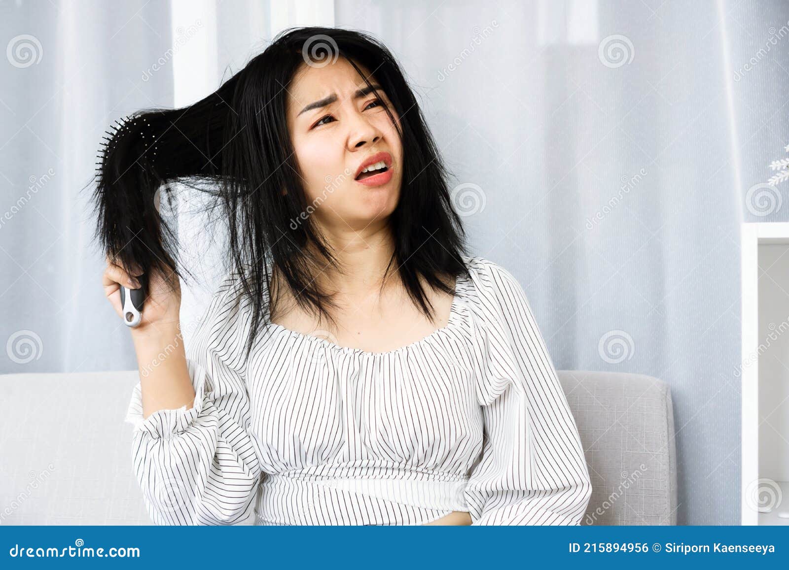 upset asian woman using comp brushing her dry ,damaged hair unhappy with messy hair