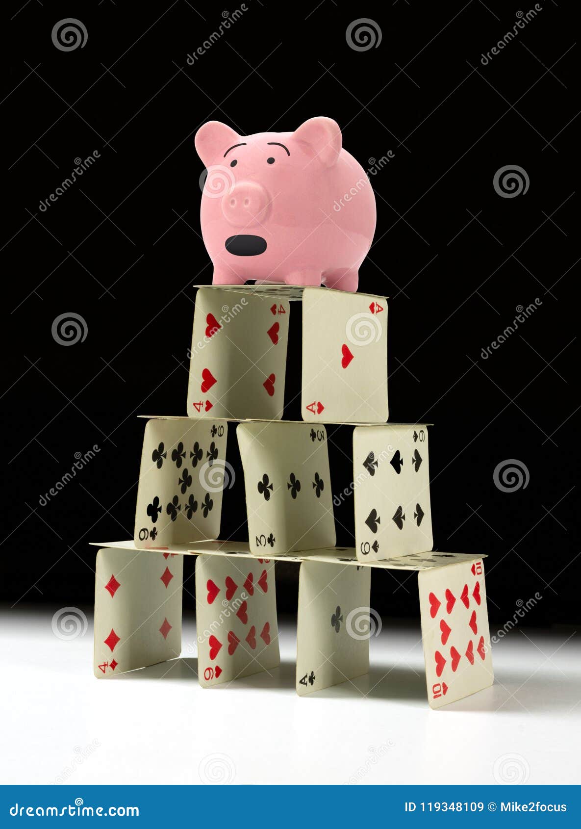 upset piggy bank standing on fragile shaky house of cards with a dark background