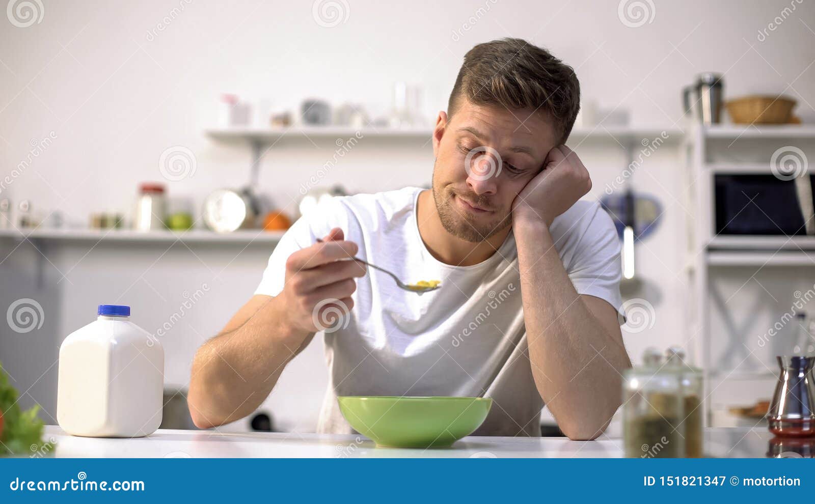 upset single man eating tasteless cereals for breakfast, lack of appetite