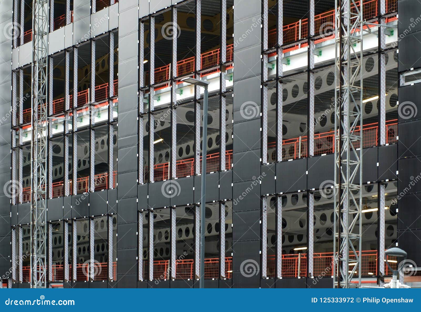 urban construction site with cladding being fastened to the metal framework of a large commercial development with orange fence