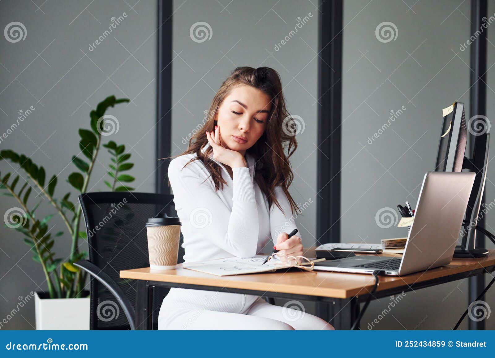 Young adult woman in formal clothes is indoors against grey