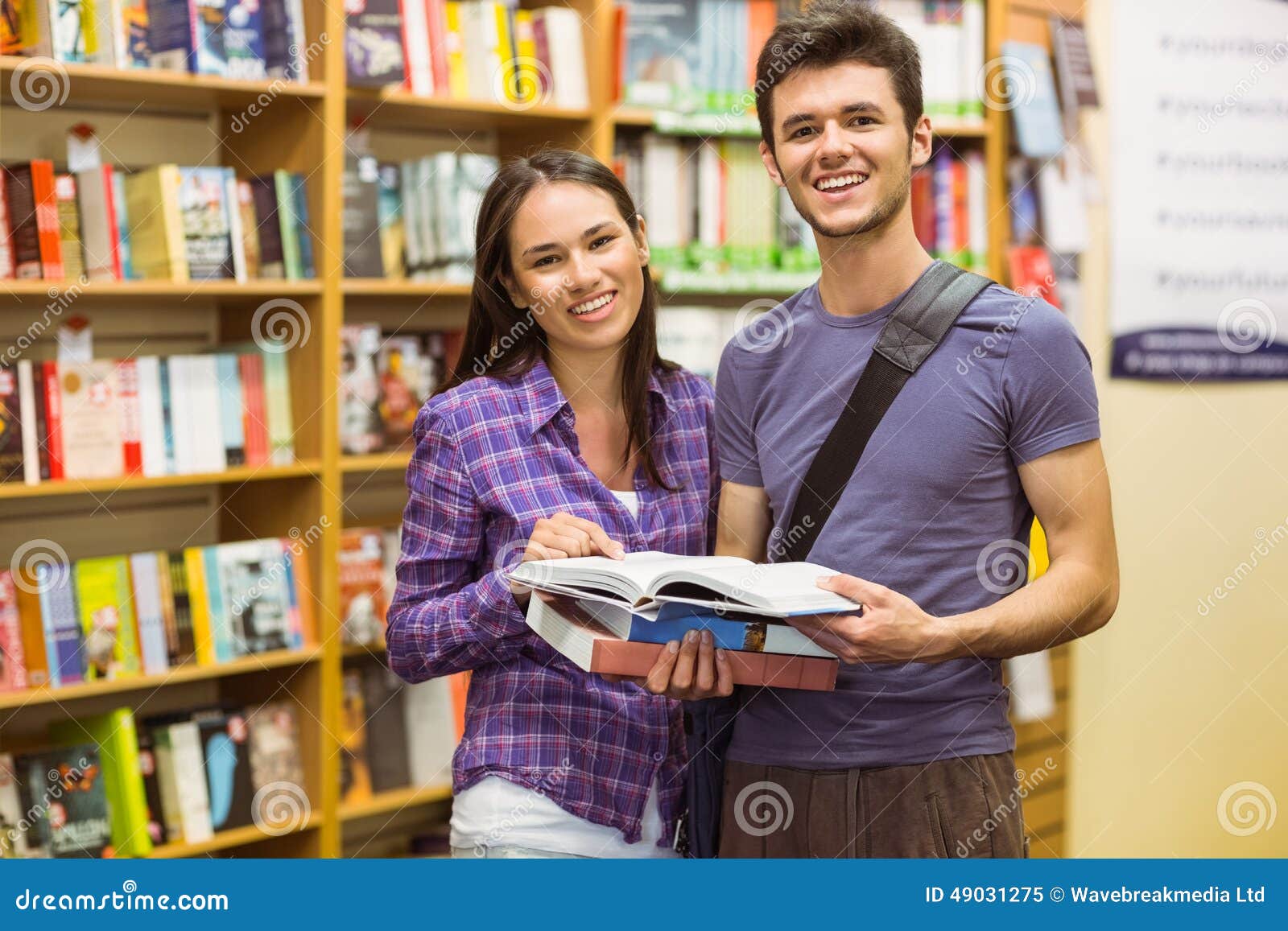 Uśmiechniętych przyjaciół mienia studencki podręcznik w bookcase przy uniwersytetem