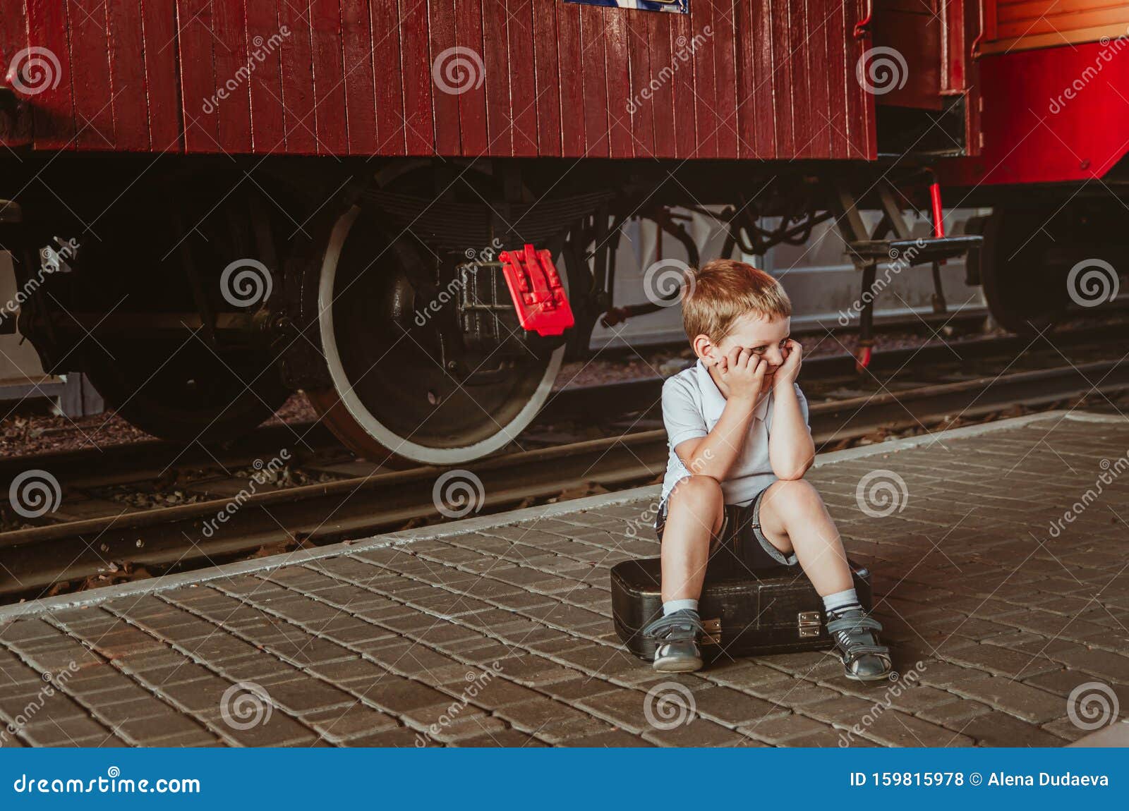 Vacaciones Con Niños Un Niño Sentado En Una Maleta En El Andén En La  Estación De Tren Un Tren Está Esperando, Es Aburrido Para él Foto de  archivo - Imagen de feliz,