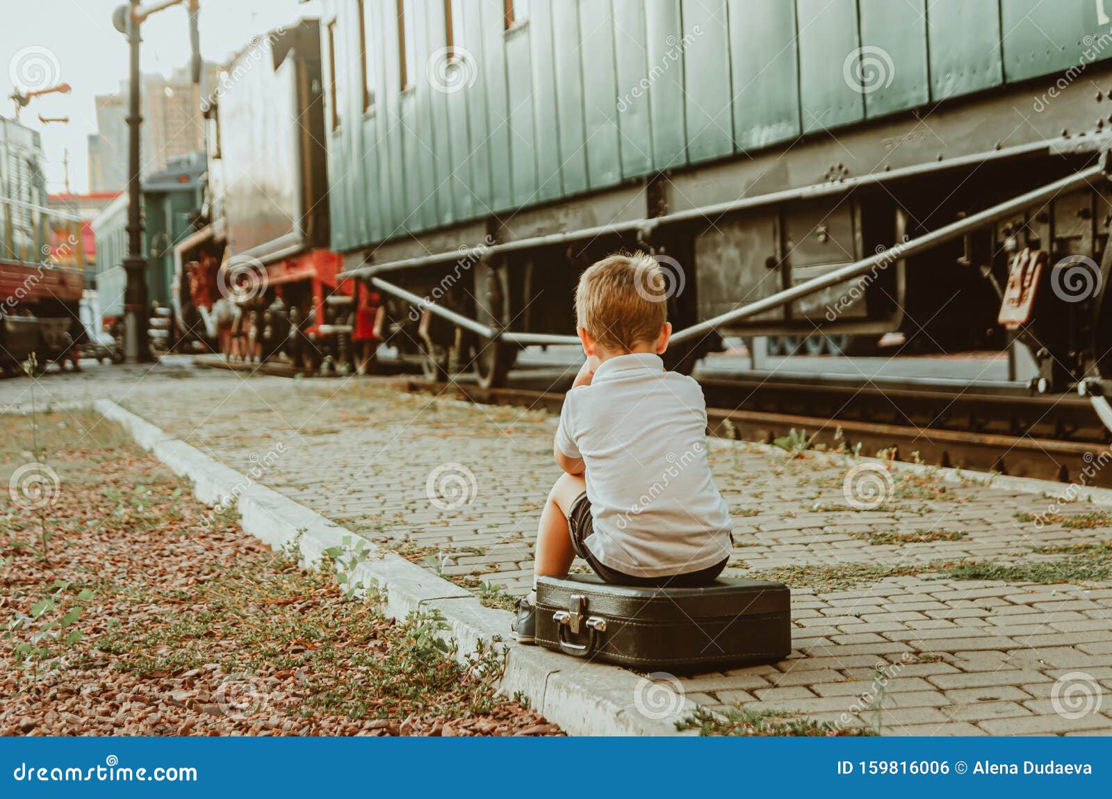 Vacaciones Con Niños Un Niño Sentado En Una Maleta En El Andén En La  Estación De Tren Un Tren Está Esperando, Es Aburrido Para él Foto de  archivo - Imagen de carril,