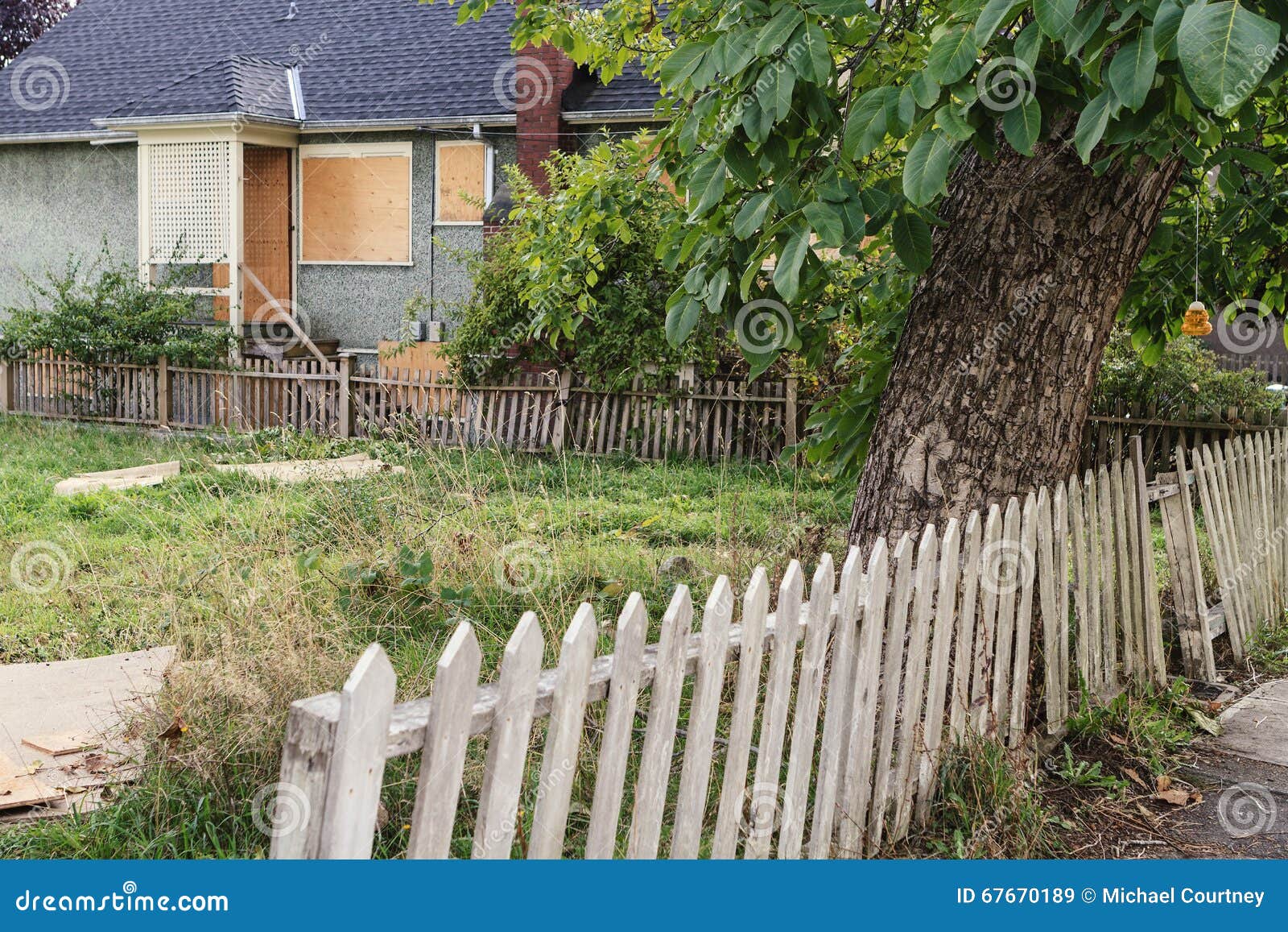 vacant unkept yard with rickety fence and boarded up house