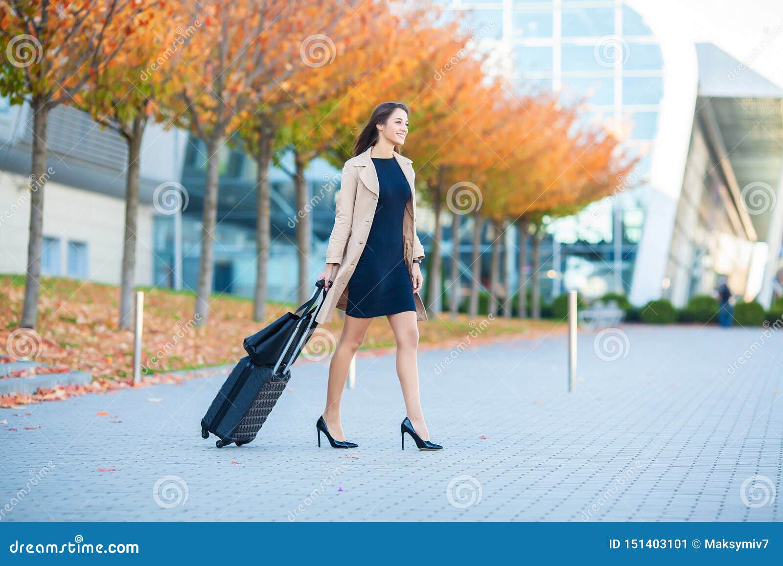 vacation. smiling female passenger proceeding to exit gate pulling suitcase through airport concourse