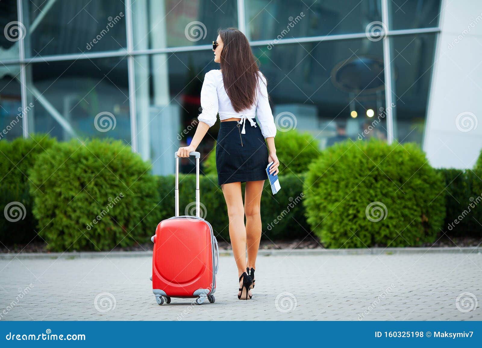 vacation. smiling female passenger proceeding to exit gate pulling suitcase through airport concourse