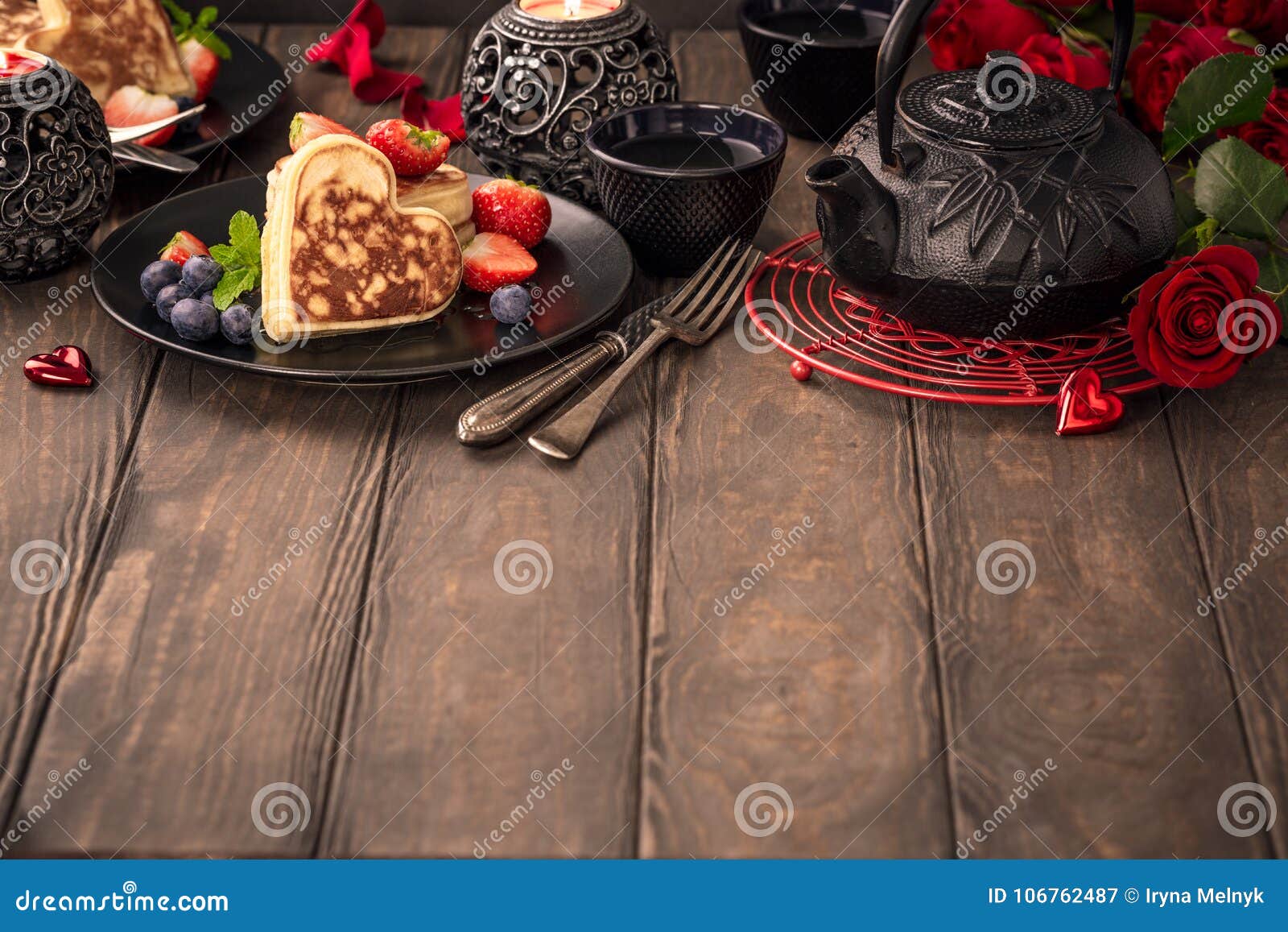 Valentinsgruß ` s Tageshintergrund mit köstlichen Pfannkuchen in der Form des Herzens, des grünen Tees, der schwarzen Teekanne, der Kerzen und der Rosen Valentinsgrußtageskonzept-Grußkarte Kopieren Sie Platz