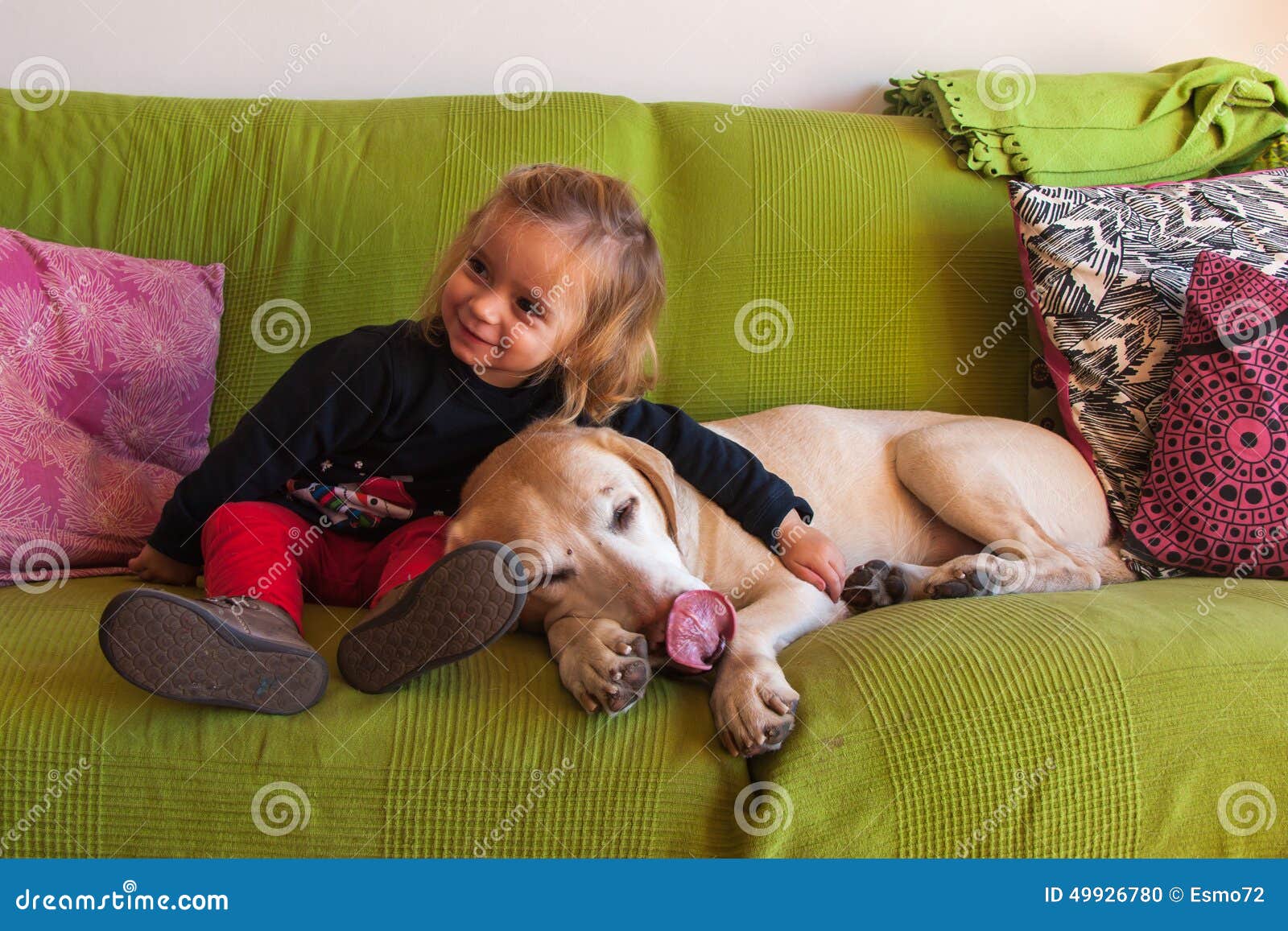 Van de twee éénjarigenmeisje en Labrador zitting in een bank thuis. Twee éénjarigenmeisje en een labrador retriever-hondzitting op een groene bus in de woonkamer thuis