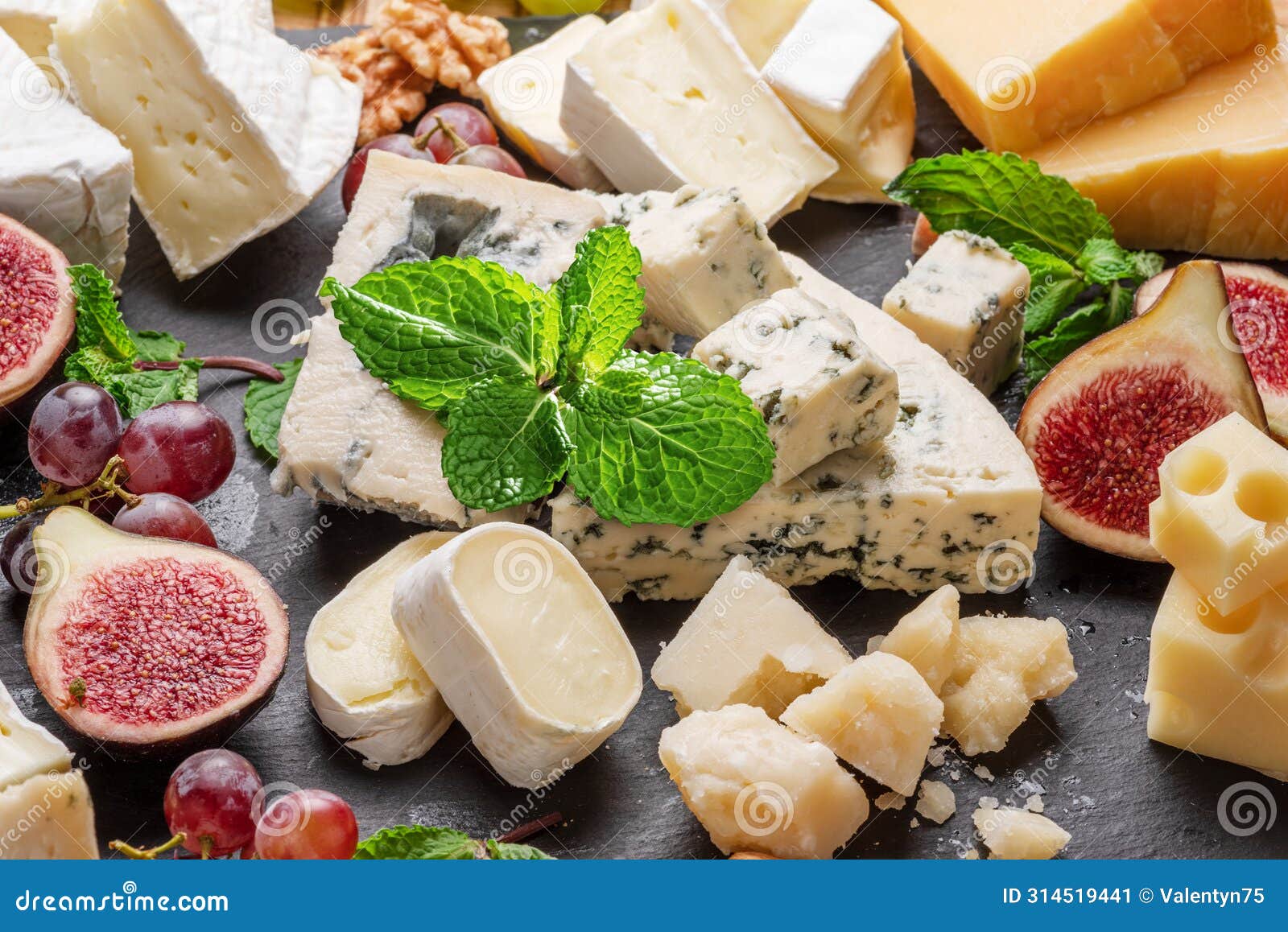 variety of sliced cheeses with fruits, mint, nuts and cheese cutting knives.