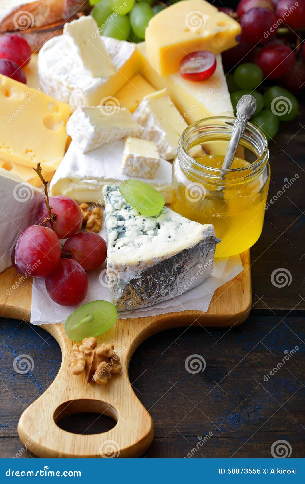 Various Types of Cheese with Grapes, Honey and Walnuts on Cutting Board