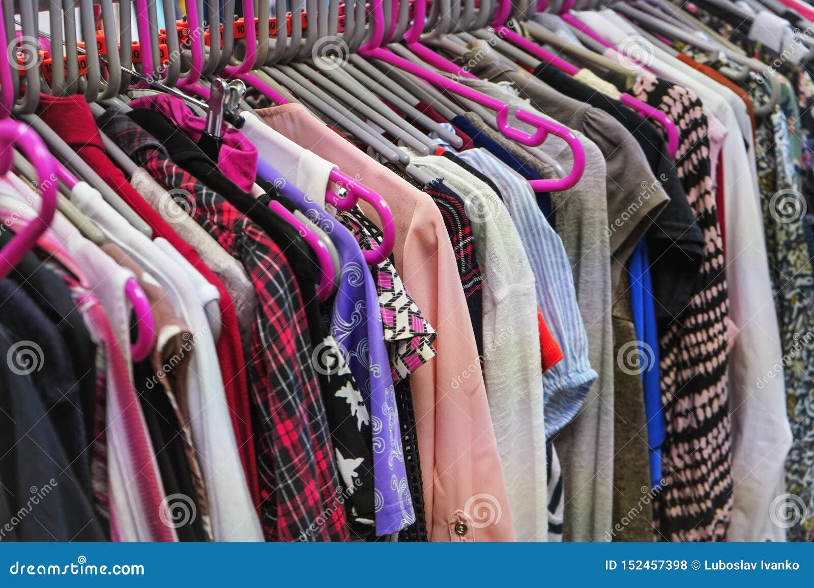 various women clothing on mostly pink coat hangers inside charity second hand thrift shop