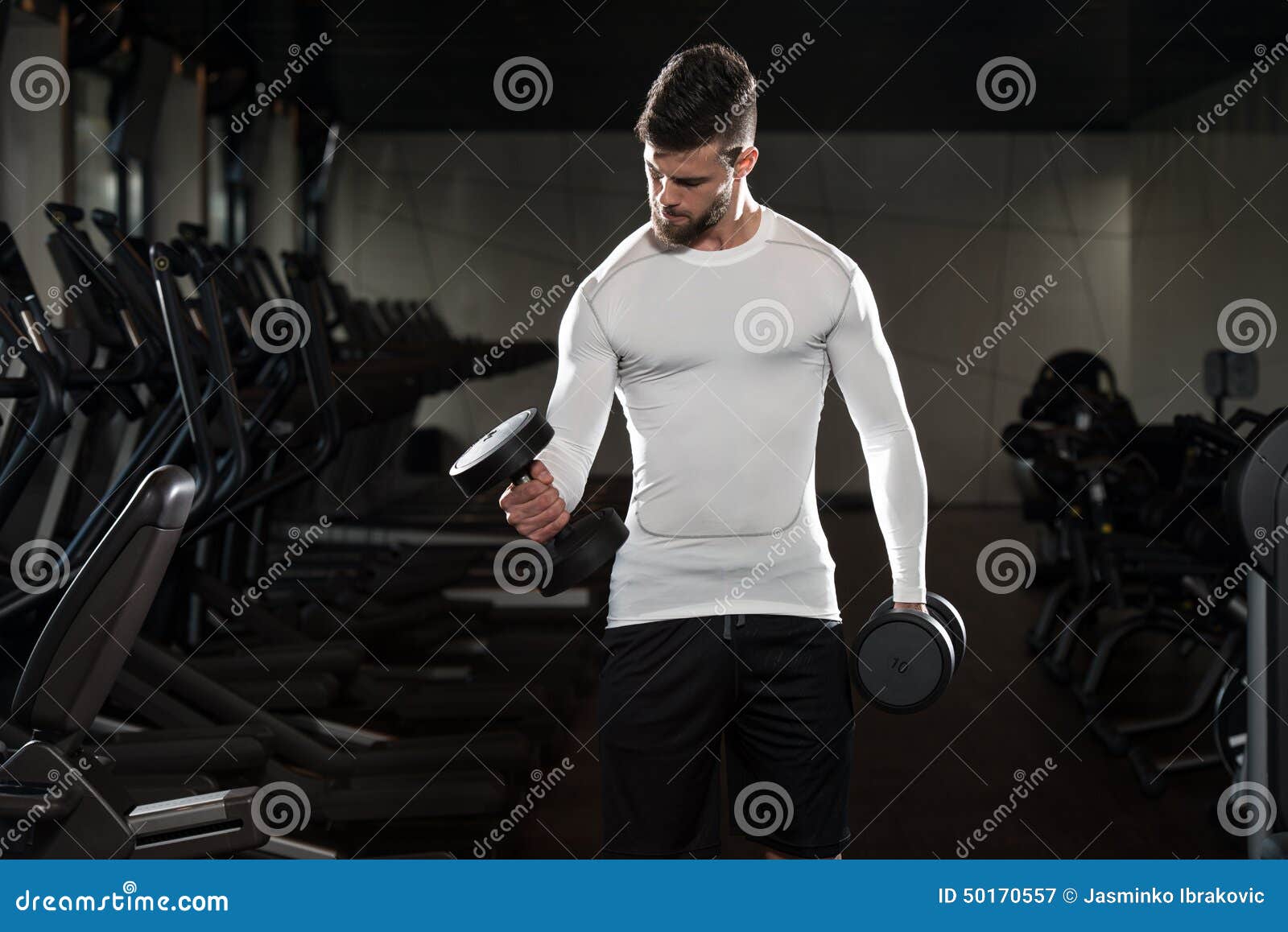 Varón joven que hace ejercicios del bíceps en el gimnasio. Bíceps con pesas de gimnasia - rizos del ejercicio del hombre joven de la concentración de la pesa de gimnasia