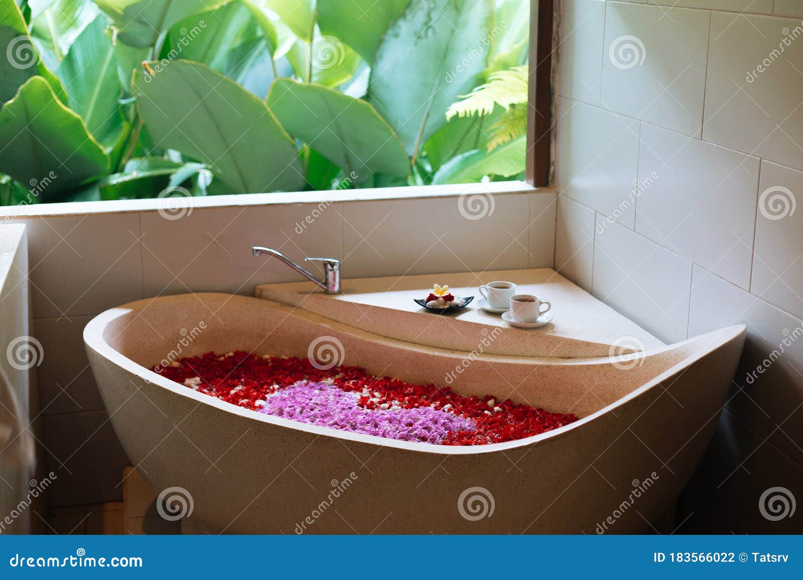 Vasca da bagno in pietra con petali di fiori a forma di cuore vicino alla  finestra con vista sulla giungla. Relax spa biologica nel lussuoso bagno di  Bali . - Foto Stock
