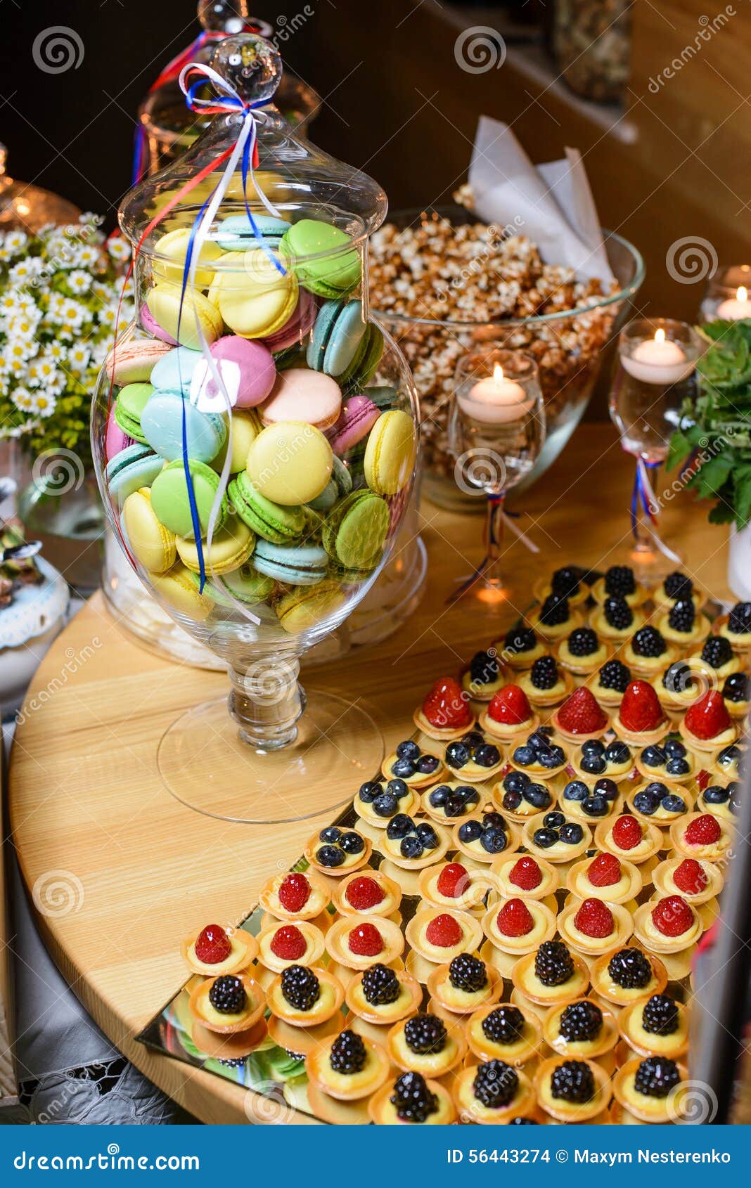 Vaso com as cookies coloridos do bolinho de amêndoa com as bagas frescas da floresta, pipoca na tabela festiva em um restaurante. Barra de chocolate em um partido no estilo francês Tabela com sobremesas diferentes e os doces decorados com flores e velas