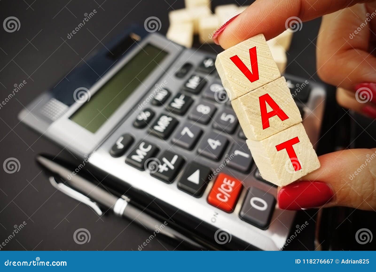 vat calculation concept with woman hand holding vat word on wooden cubes above calculator keyboard on dark background