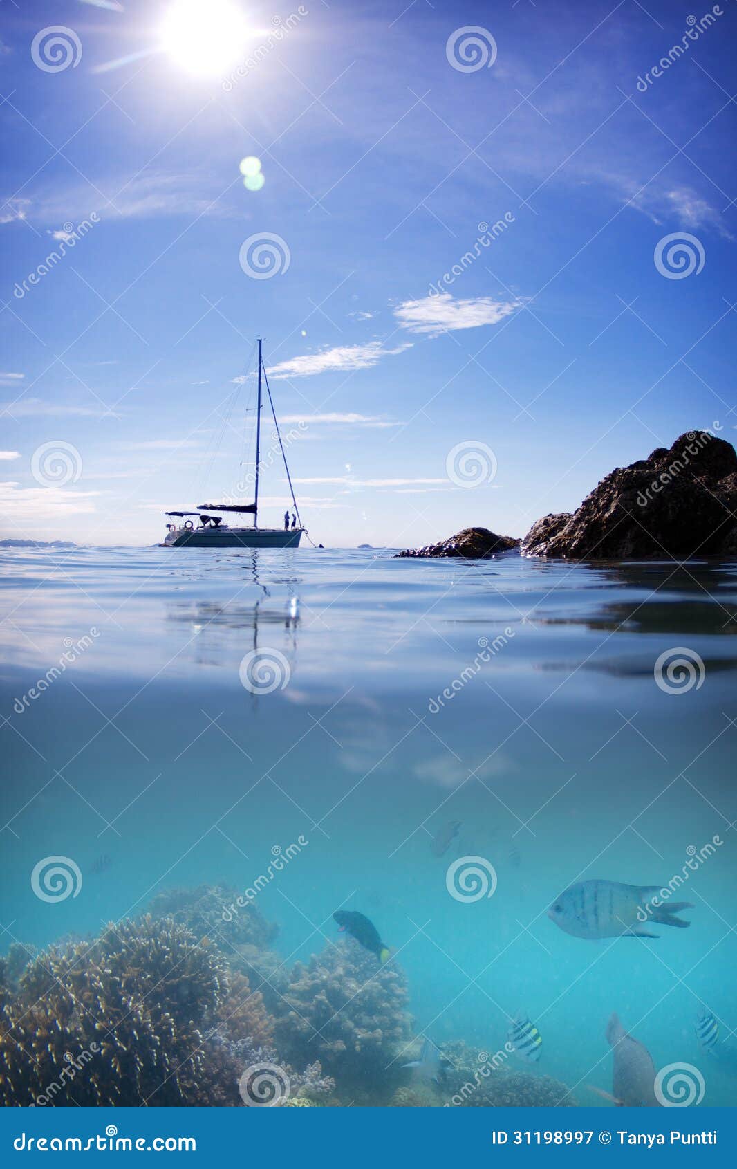 Vatten och himmel för sol för Coral Reef fiskfartyg. Splittring under och över fotografiet av en korallfeeffisk, ett förankrat fartyg, en sol, ett blått vatten och en himmel nära en pingstdagö.