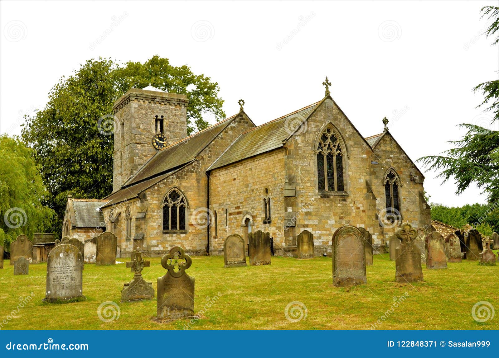 Vecchia chiesa di pietra in punti di riferimento di North Yorkshire - di Hovingham. Una vista esteriore attraverso un cimitero alla chiesa rurale in Hovingham, North Yorkshire