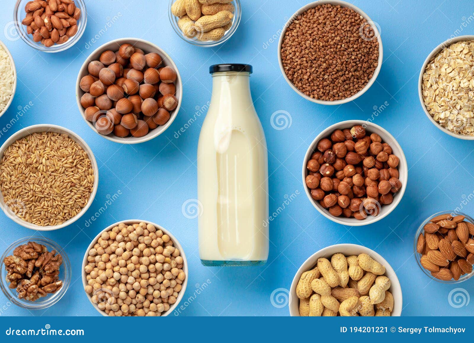 Vegetable Milk Concept with Milk Bottle and Bowls with Grains on Blue