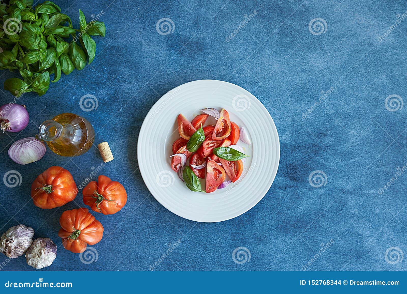 vegetable tomato salad with extra virgin olive oil, purple onion, purple garlic and basil. accompanied by a bottle of extra virgin