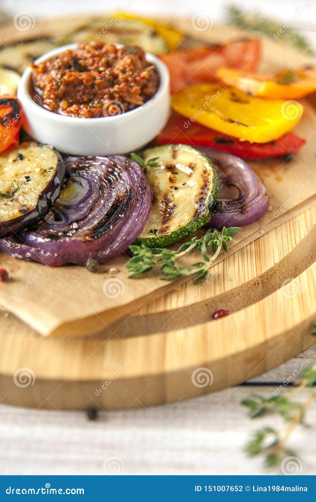 Veh?culos asados a la parilla. Verduras asadas a la parrilla con verdes picantes frescos y salsa del pesto de tomates rojos Guarnición para las dietas quetogénicas y del paleo Porción grande en una placa de madera en un estilo rústico Ciérrese para arriba y orientación vertical Foco selectivo