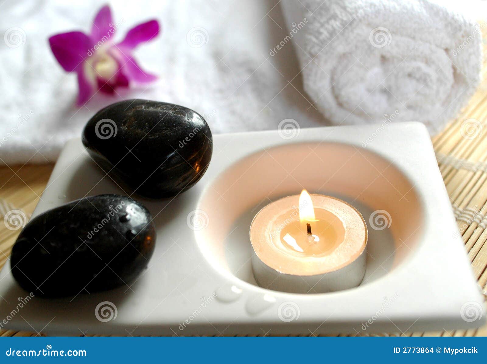 Vela aromática, piedras, orquídea y una toalla blanca