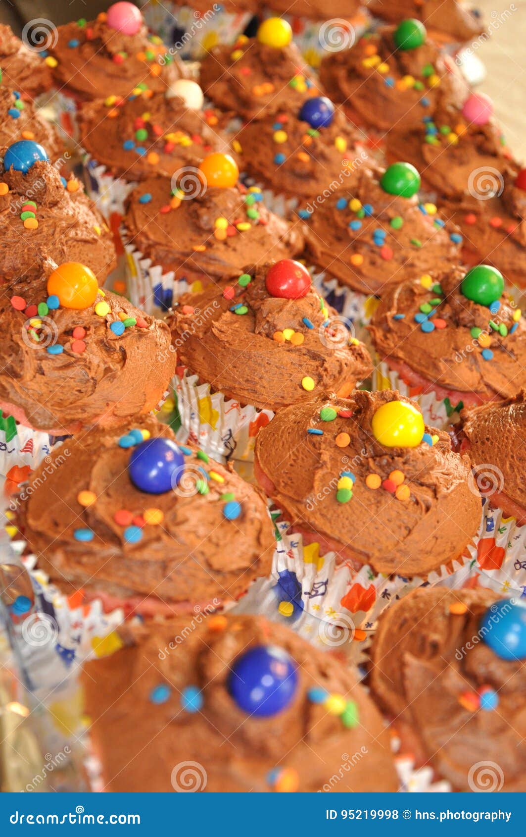 Een dienblad van chocolade-berijpte en confetti-bestrooide verjaardag cupcakes wacht op een partij Elke cupcake wordt bedekt met een kleurrijke gumball