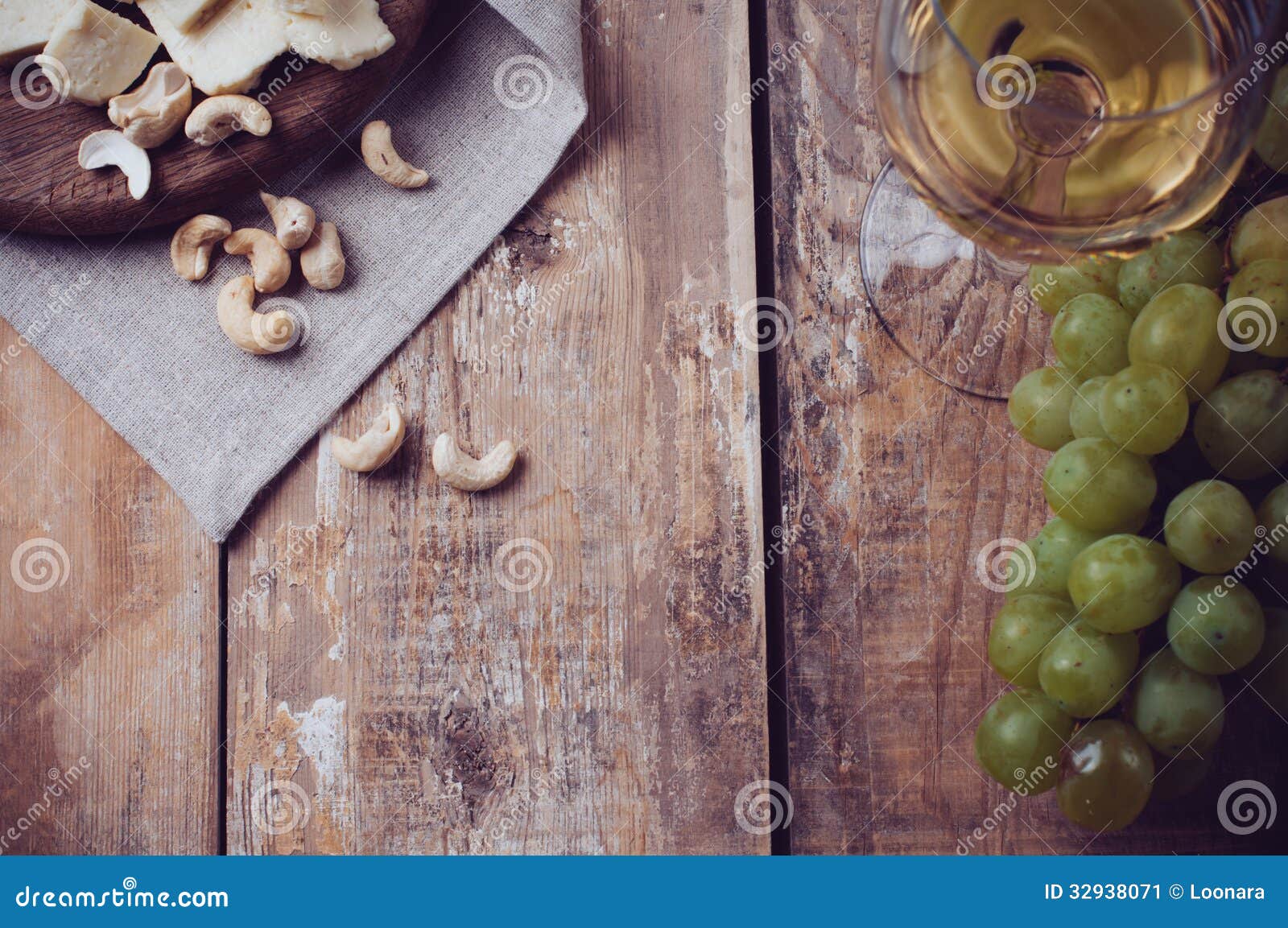 Un verre de vin blanc, de raisins, de noix de cajou et de fromage à pâte molle sur un conseil en bois, fond rustique de style
