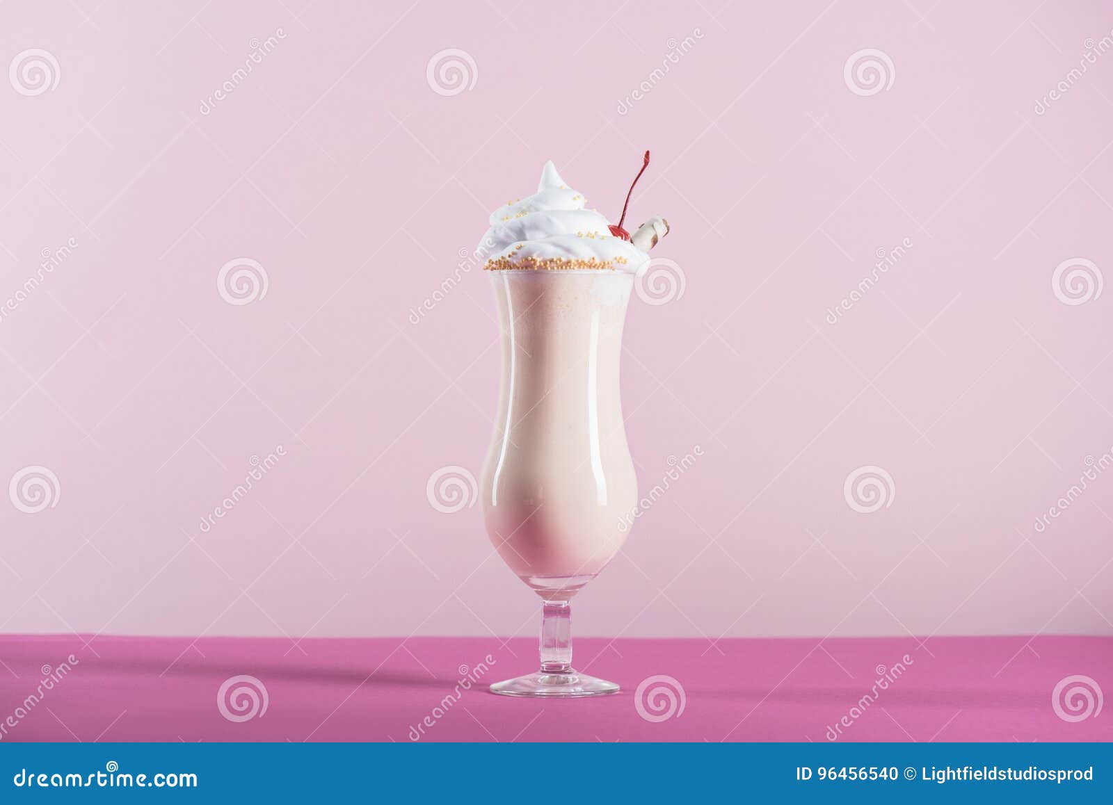 Verse milkshake met room en kers op bovenkant in glas op roze tafelblad