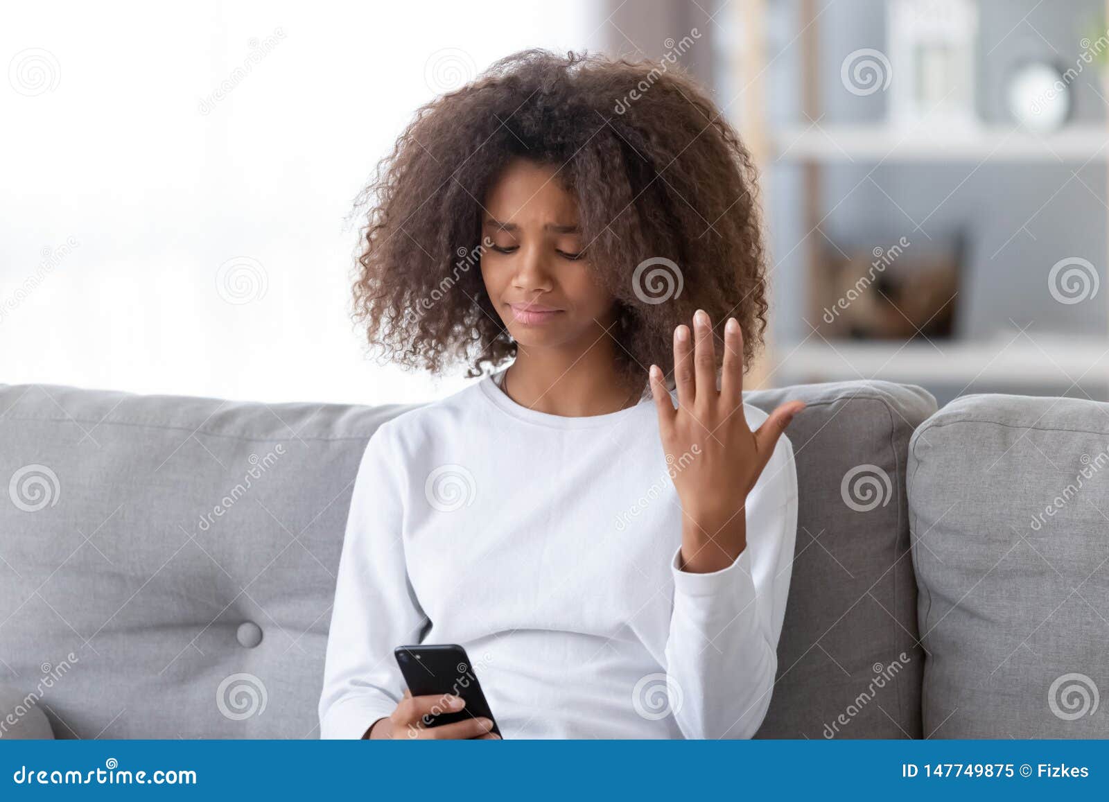 Verstoor Afrikaans Amerikaans tienermeisje gebruikend telefoon, ontvangen onplezierig bericht, die op laag zitten, voelend ongelukkig, tienerprobleemconcept, eerste liefde en jaloersheid, gebroken vriendschap, slecht nieuws