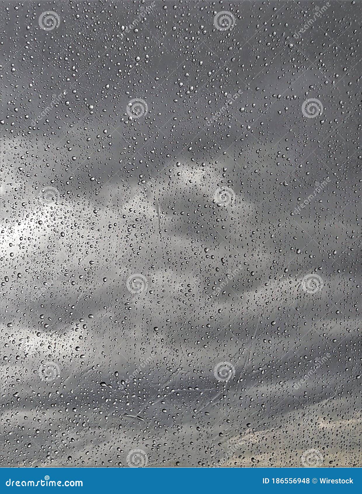 vertical closeup of raindrops on the window with a cloudy sky on the blurry background