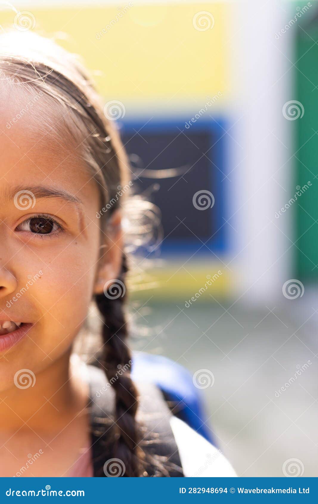 vertical half face portrait of smiling cauasian ary schoolgirl in schoolyard, copy space