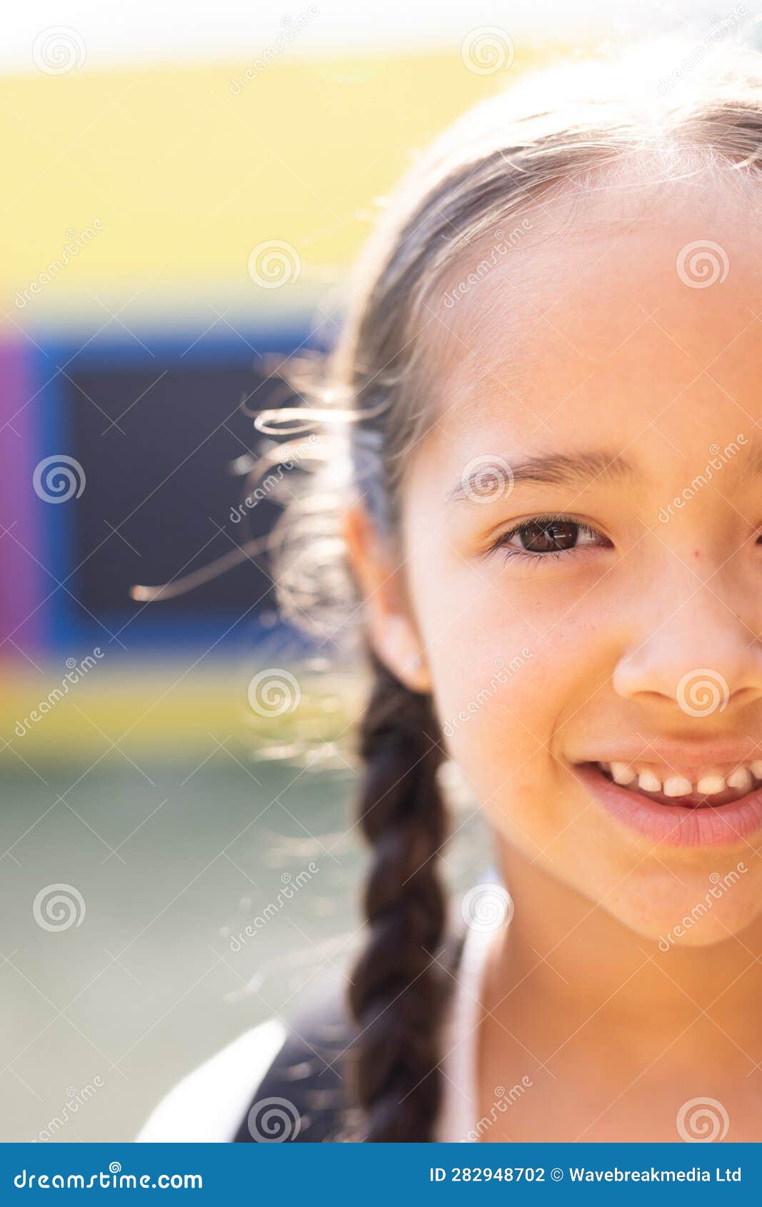 vertical half face portrait of smiling cauasian ary schoolgirl in schoolyard, copy space