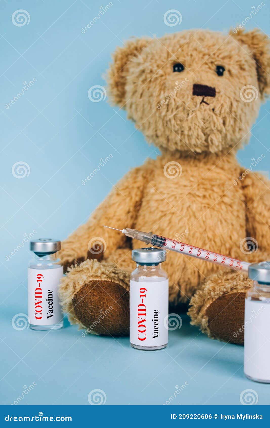 vertical image of teddy bear with vial dose of covid-19 vaccine with syringe against blue background with copy space -