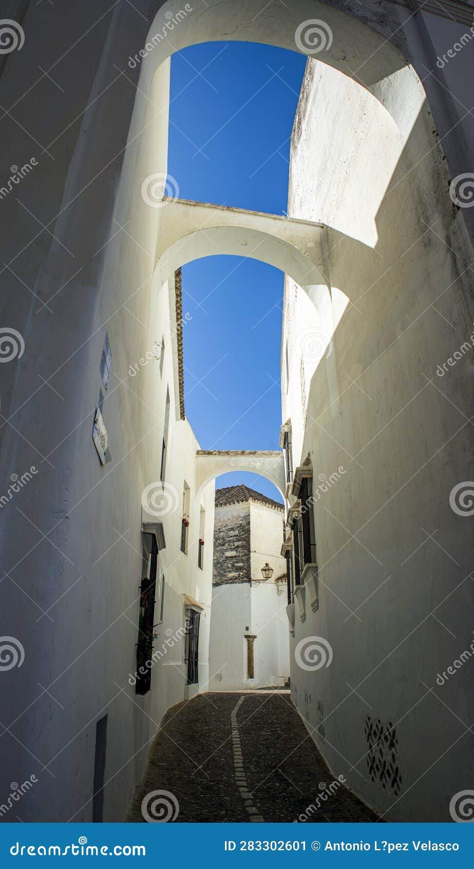 vertical pictura of a narrow white alley of the old quarter of arcos de la frontera, cadiz, andalusia, spain