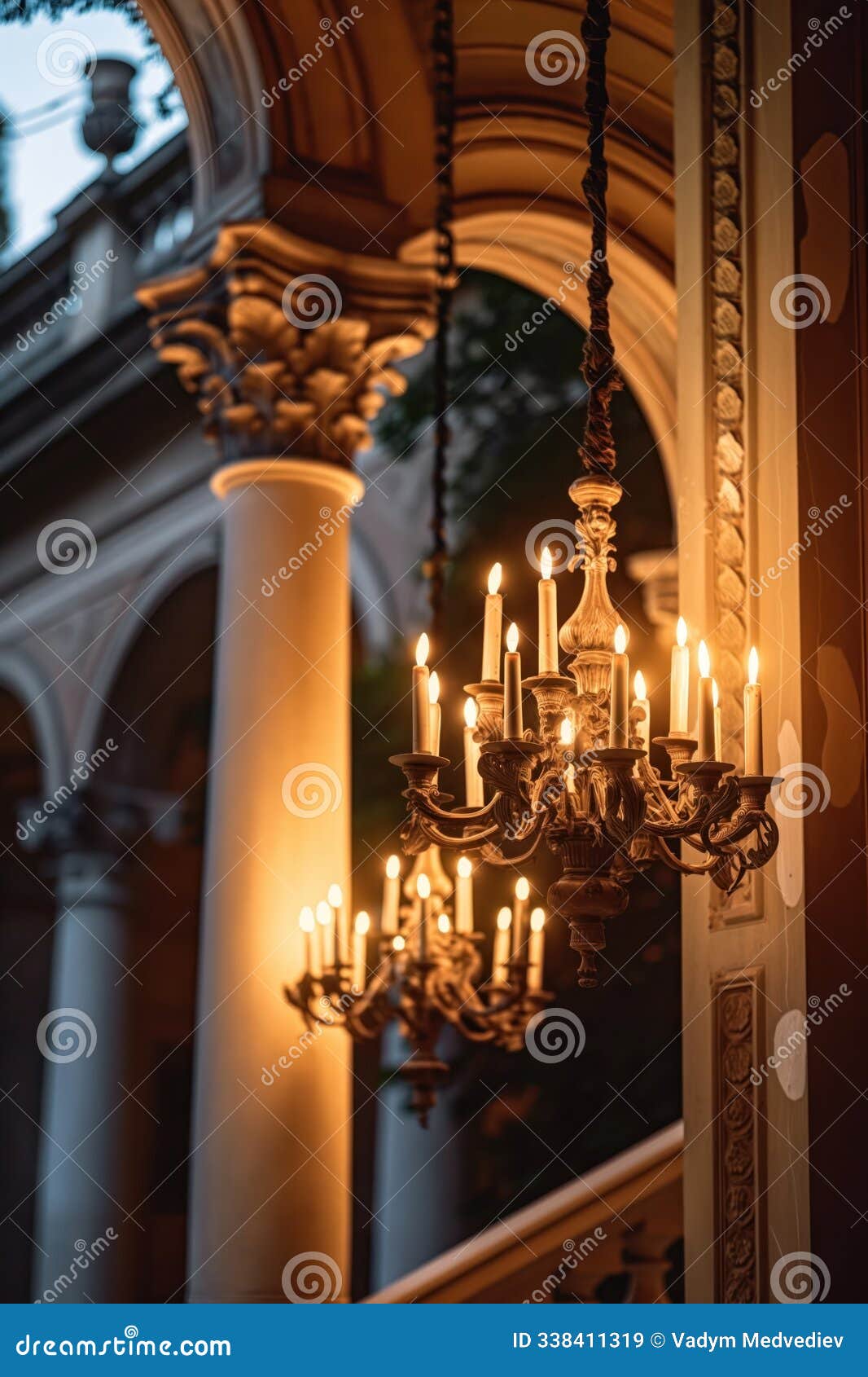 vertical shot of antique chandelier with candles illuminating grand building with ornate columns. beautiful architecture features