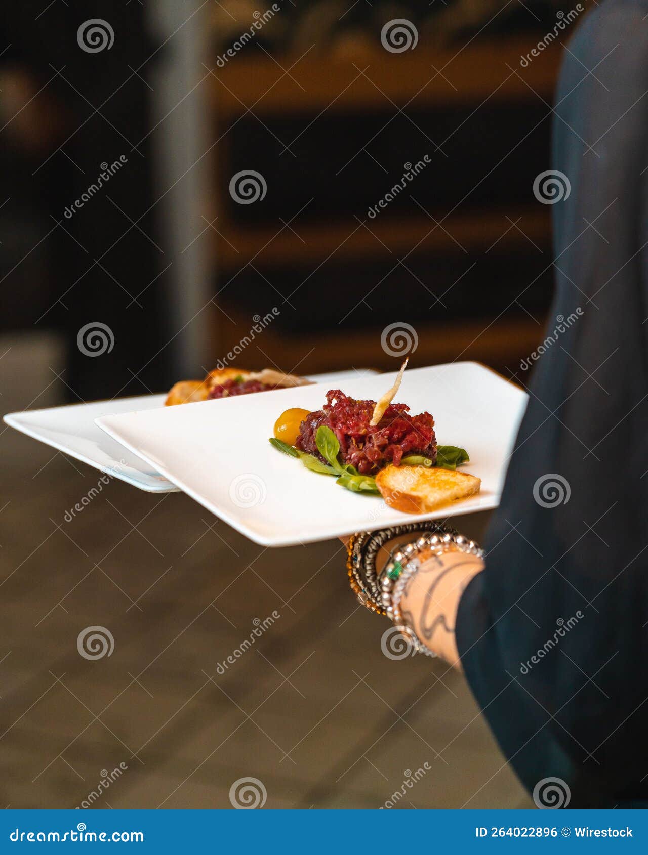 vertical shot of a person holding a plate of beef tartare against the  background