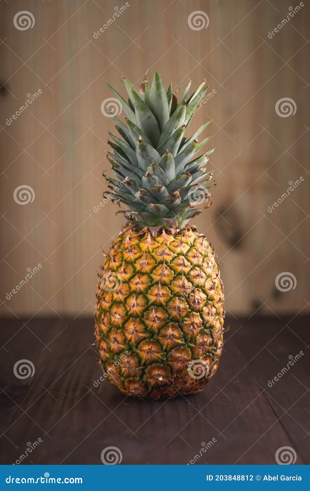 vertical shot of a ripe tropical pinapple on a wooden table with a wooden background.