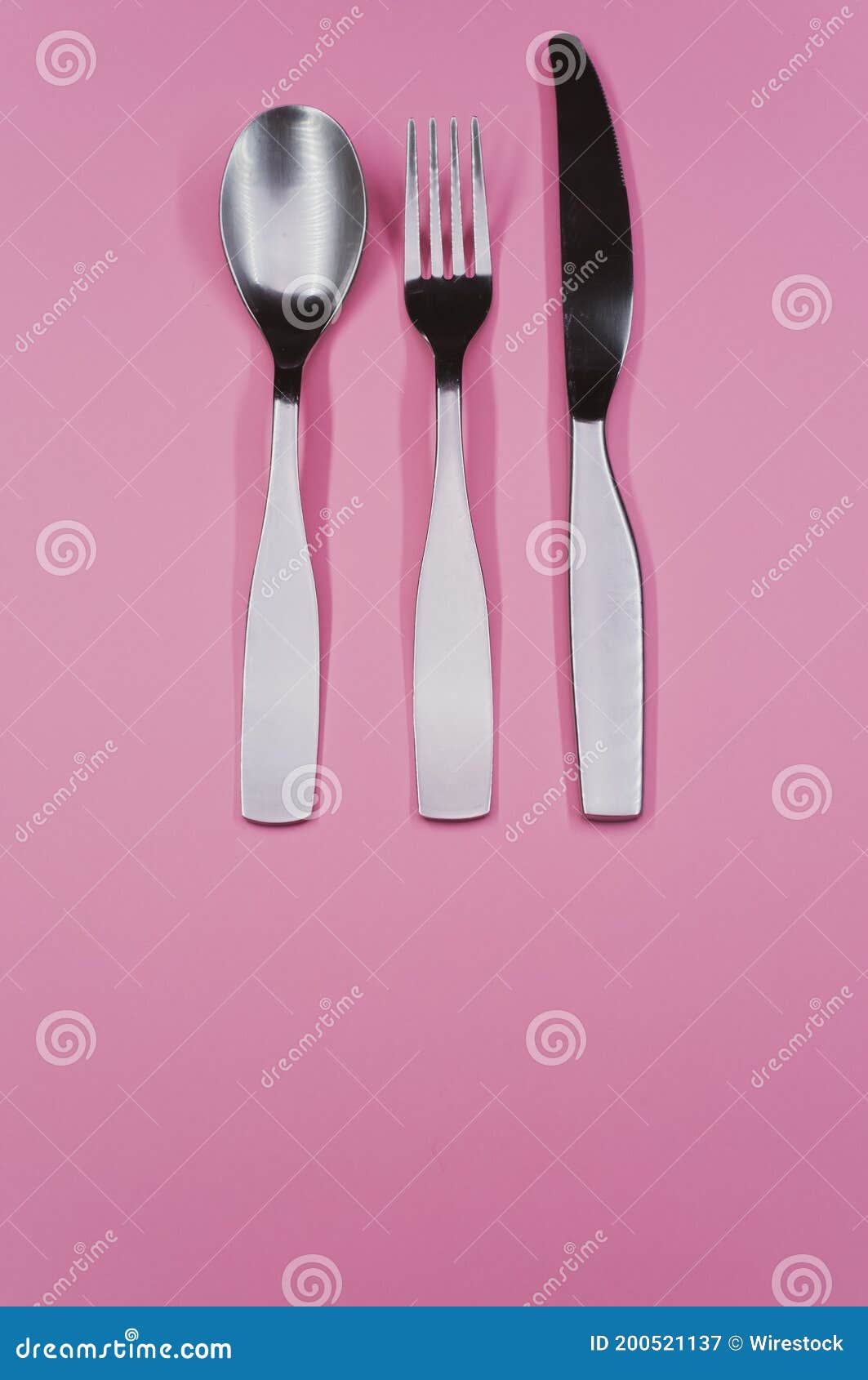 Vertical Shot of a Spoon, Fork, and a Knife on a Pink Surface Stock