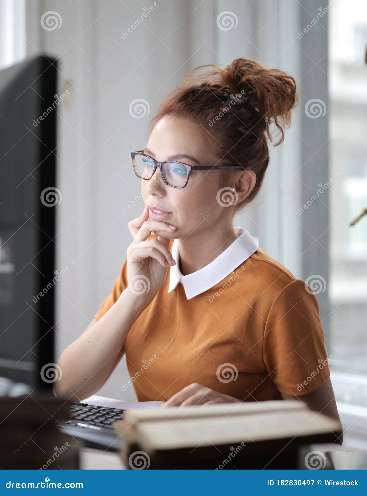 Vertical Shot of a Thoughtful Young Female with Glasses Working on a Computer Under the Lights