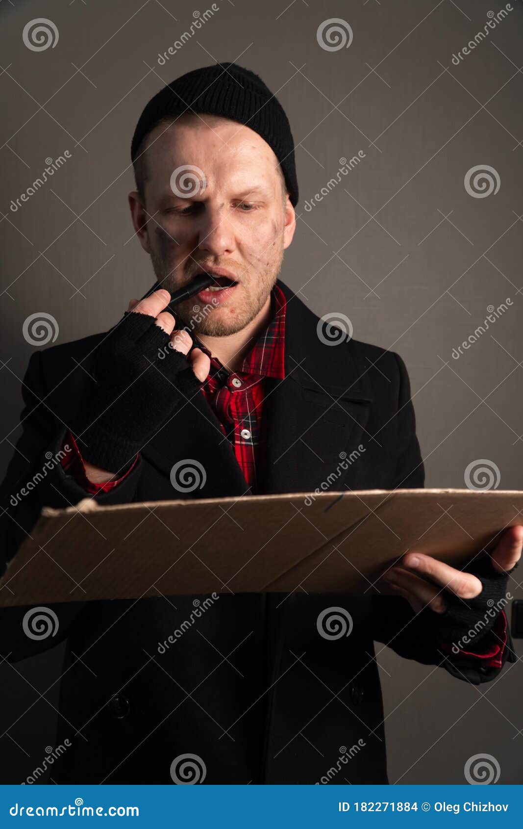 vertical shot of a young man who holds a felttip pen in his mouth to write text on cardboard. begging concept
